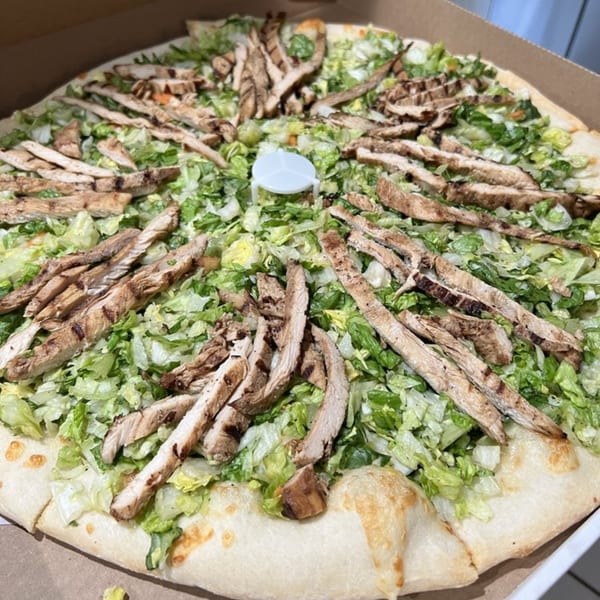 A large pizza topped with shredded lettuce and grilled chicken strips in a cardboard box.
