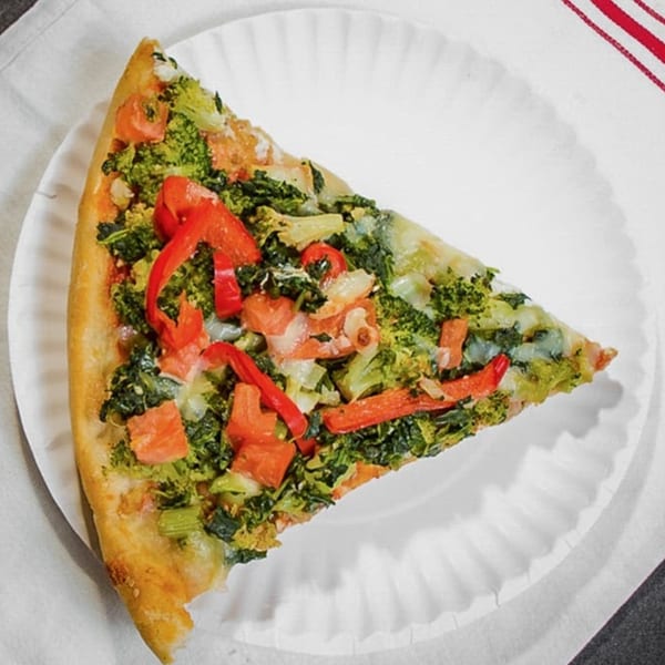 A slice of Touch of Italy's vegetable pizza, topped with broccoli, red peppers, and tomatoes.