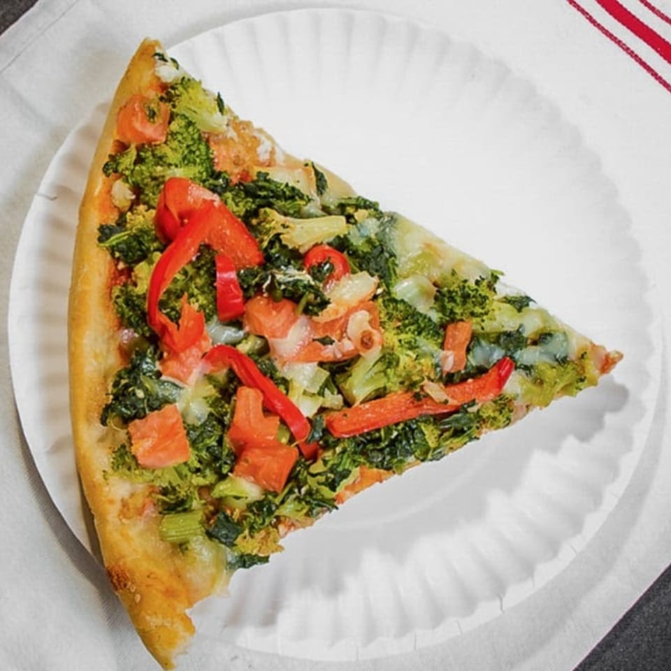 A slice of Touch of Italy's vegetable pizza, topped with broccoli, red peppers, and tomatoes.