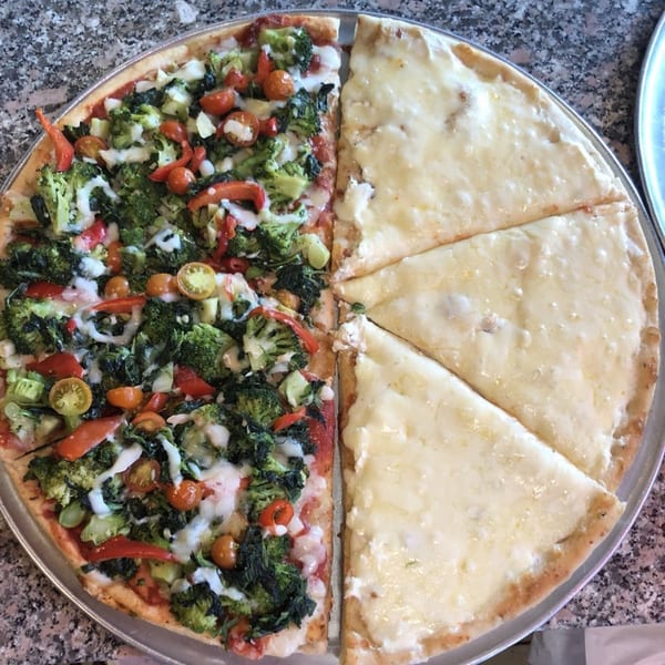 Half a pizza with broccoli, tomatoes, and cheese, and the other half with plain cheese.