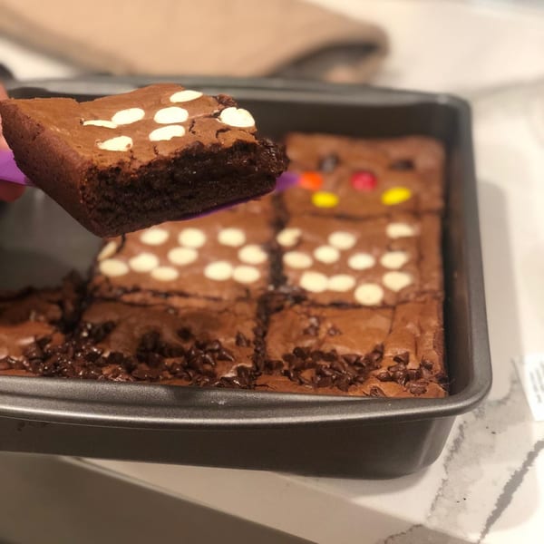 A hand lifts a chocolate brownie with white chocolate chips from a pan of brownies.