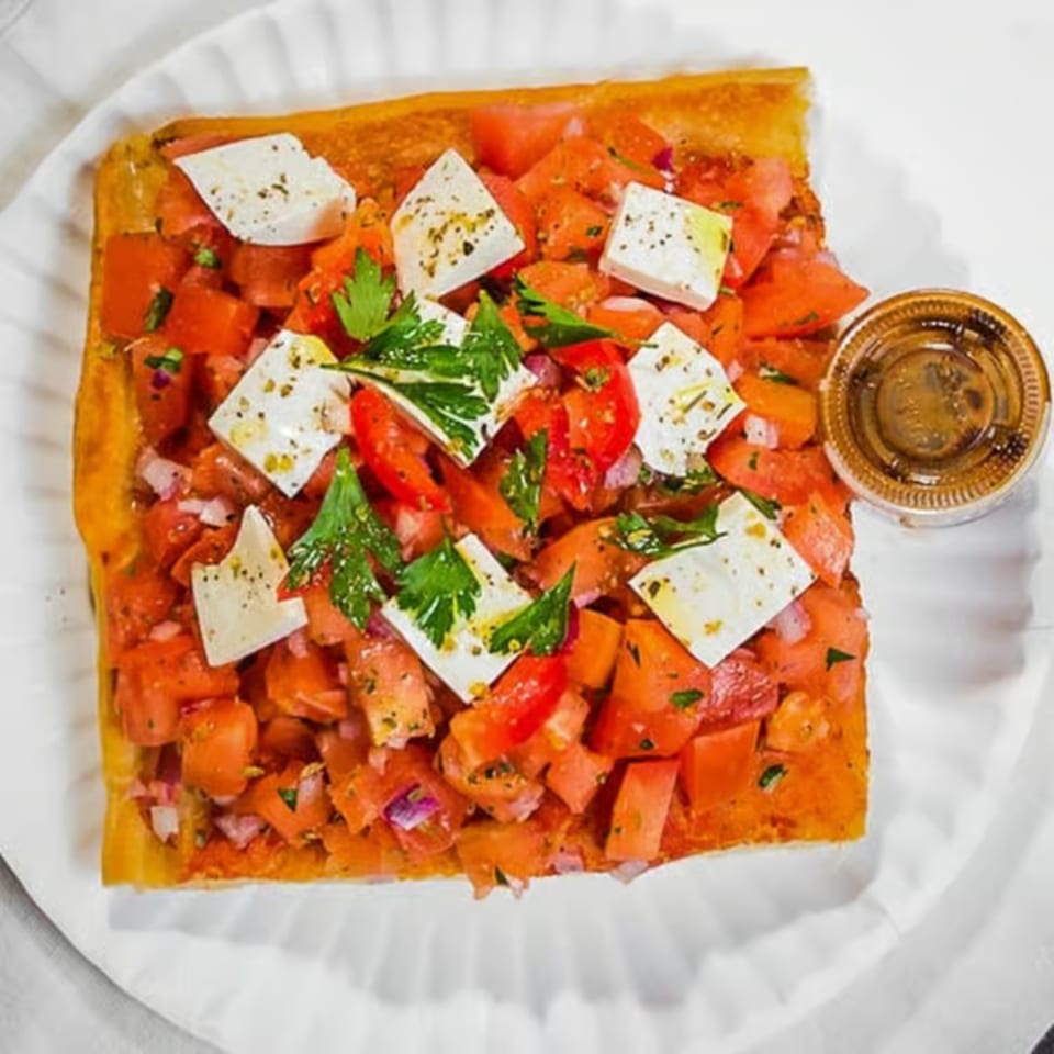 Square Italian bruschetta with diced tomatoes, feta cheese, and parsley, served with a side of sauce.